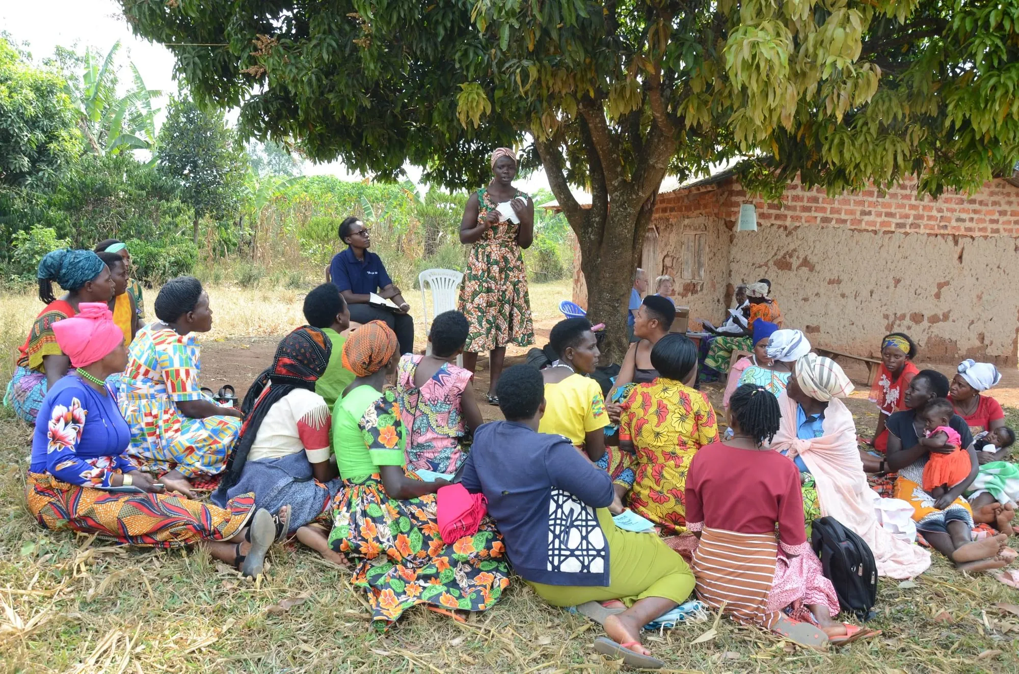 Community members in Kiswa, Uganda gathered under a tree for a project meeting