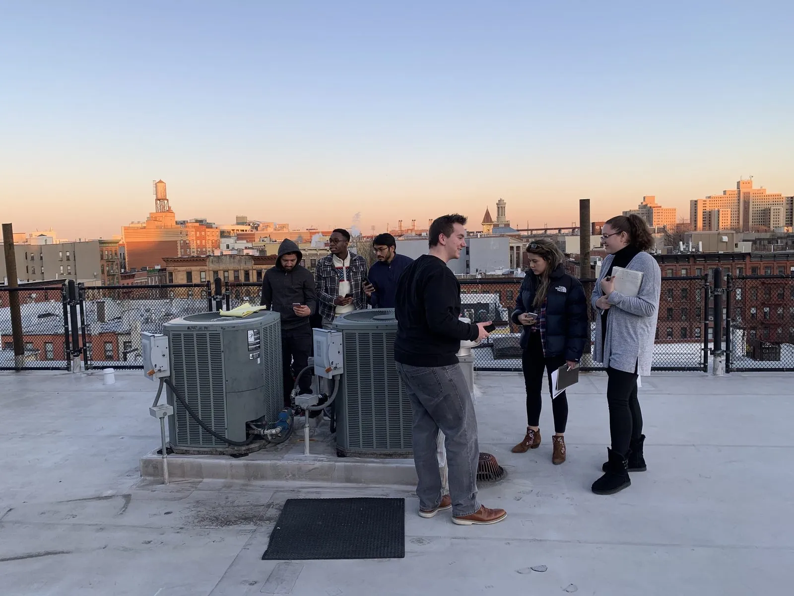 EWB-CCNY members surveying rooftop mechanical equipment at sunset over Manhattan